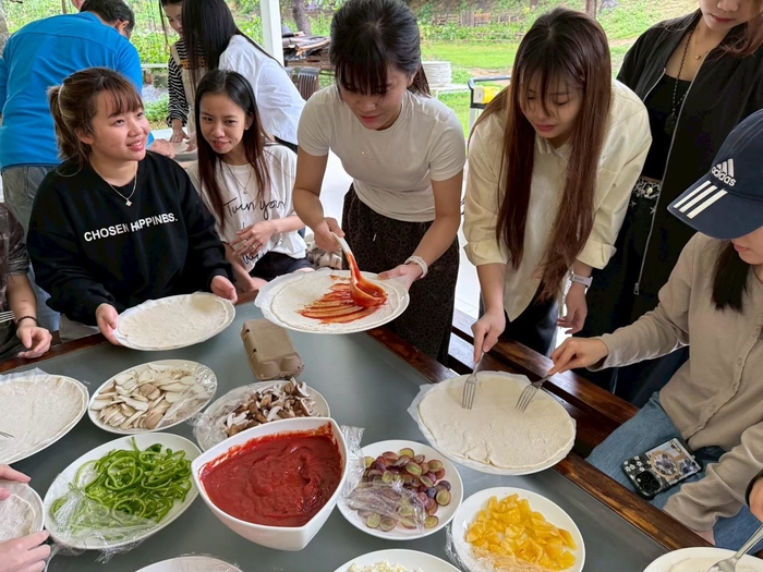 學生依照個人喜好塗抹醬料、鋪放起司及各式配料，合作完成專屬創意披薩，培養團隊合作與創意思維。圖片